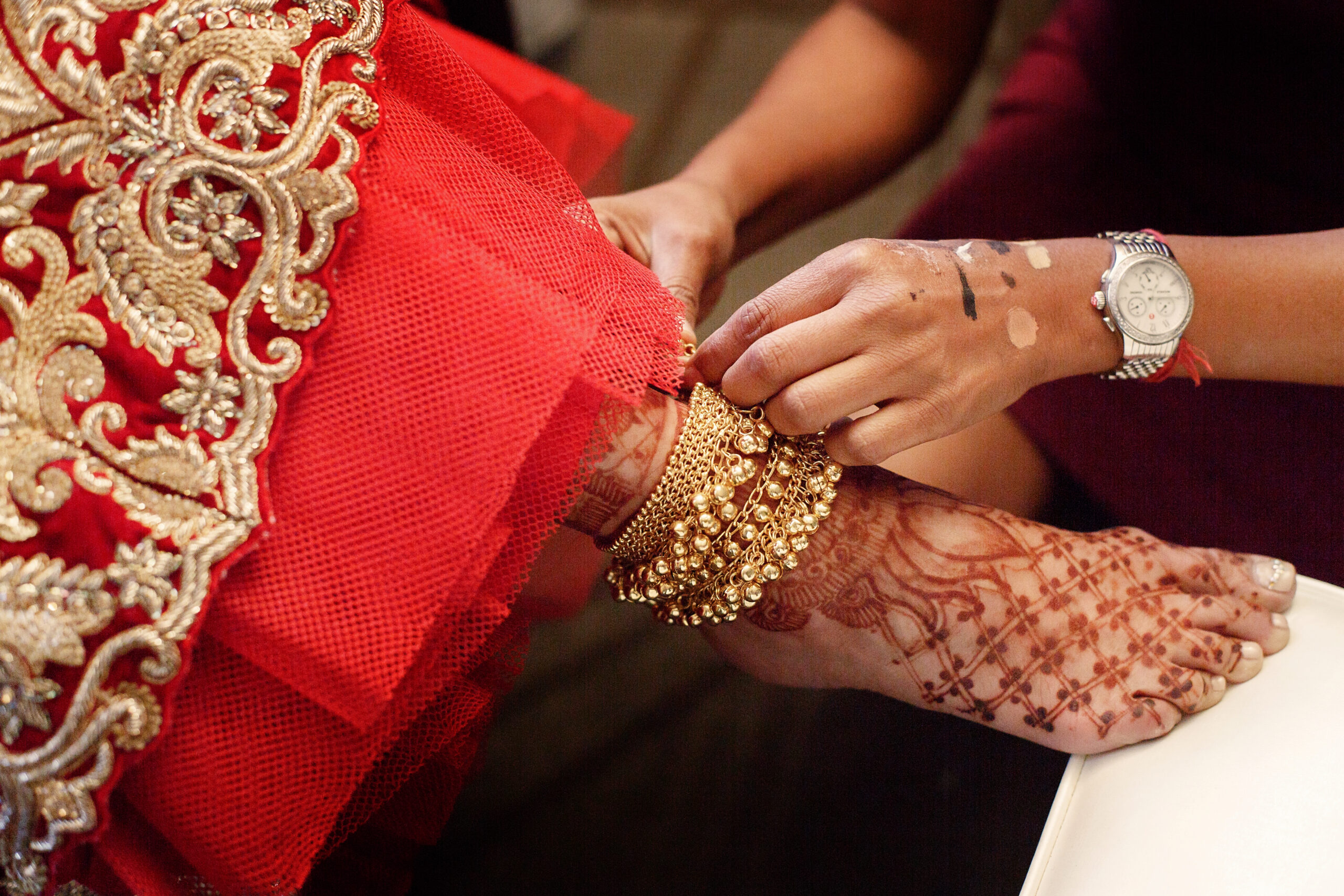 woman puts golden bracelet with bells on bride's leg painted wit